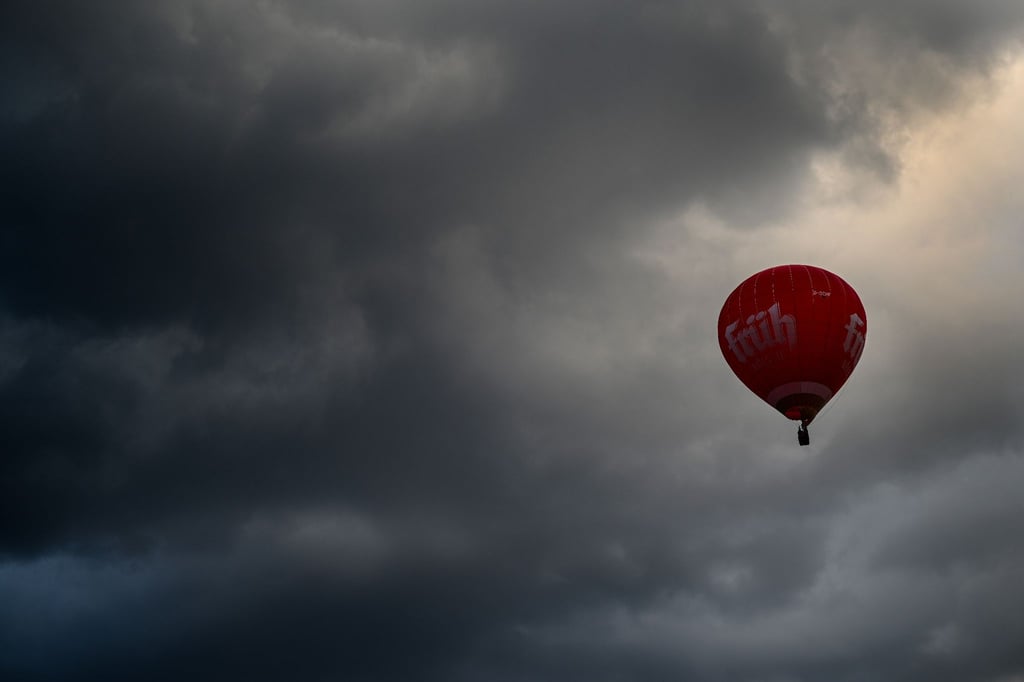 Ein roter Heißluftballon fährt vor den Wolken.