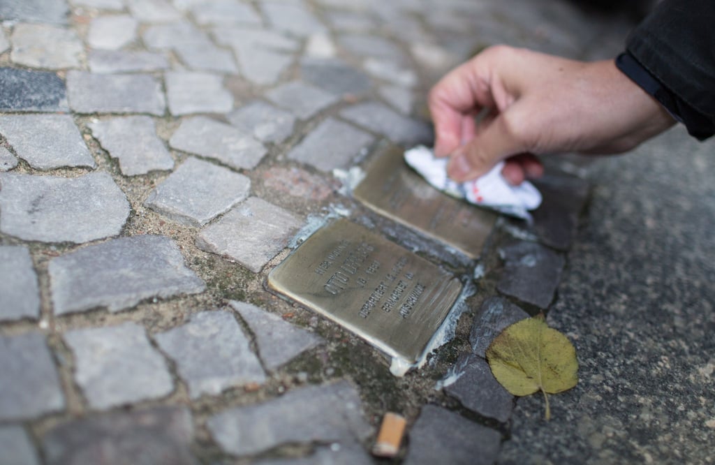 Ein Mann putzt in Berlin einen "Stolperstein".