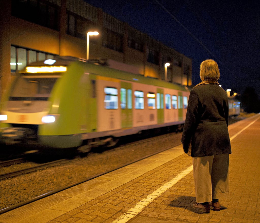 Eine Frau steht allein nachts auf einem Bahnsteig.