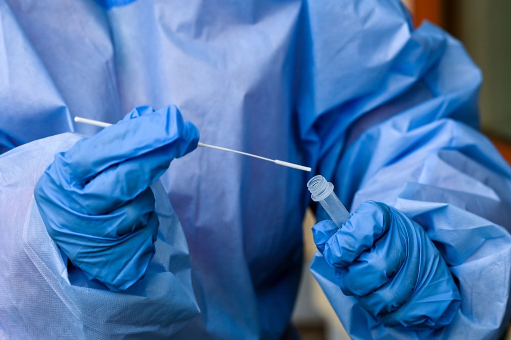Eine Krankenschwester steckt ein Abstrichstäbchen in die Flüssigkeit eines Corona-Schnelltests.