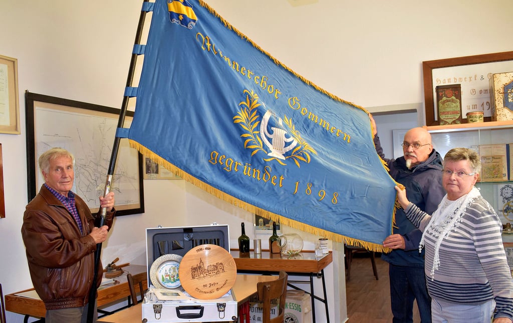 Eckhard Blumenthal (l.) und Michael Wohlfahrt überreichten an Karin Gust, Vorsitzende des Heimatvereins, die Fahne des Männerchores Gommern. Zum Jahresende löst sich der Chor auf. Einen Koffer voll mit den wichtigsten Unterlagen und Exponaten wie Erinnerungstellern, einem Chorfoto und Wimpel. übernahm der Verein ebenfalls.