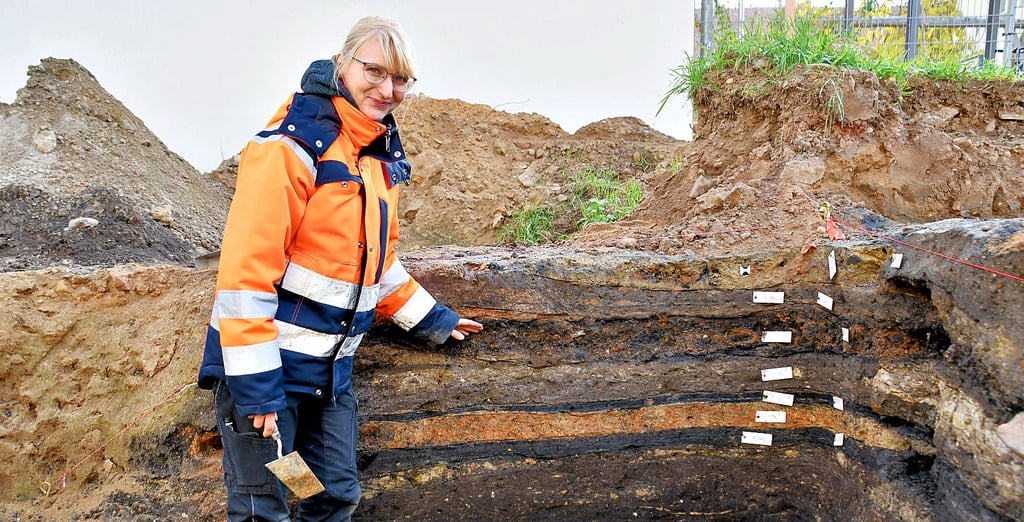 Anja Tuschwitz vom Landesamt für Denkmalpflege und Archäologie in Sachsen-Anhalt zeigt die Bodenschichten, die sie und die Grabungshelfer freigelegt haben. Sie weist auf eine alte Brandschicht hin.