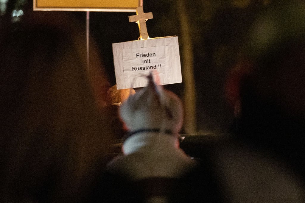 Ein Mann mit einer weißen Mütze mit rot und blauen Bändern daran nimmt an der Montagsdemonstration teil.