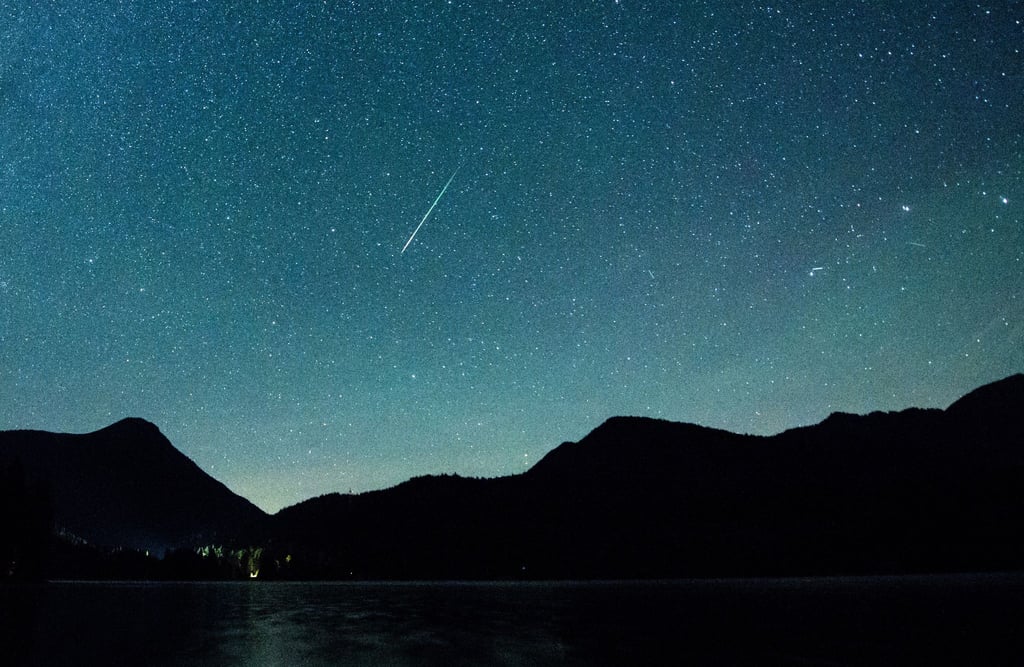 Eine Sternschnuppe leuchtet neben der Milchstraße am Himmel über dem Walchensee.