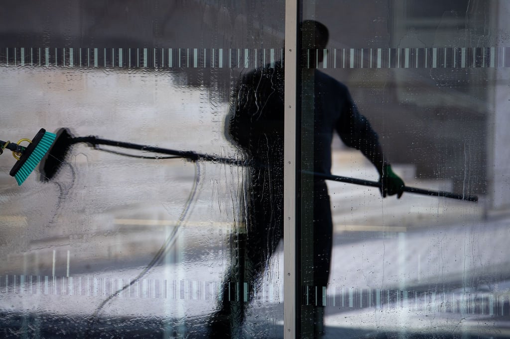 Die Silhouette eines Gebäudereinigers spiegelt sich in einer Fensterfront.
