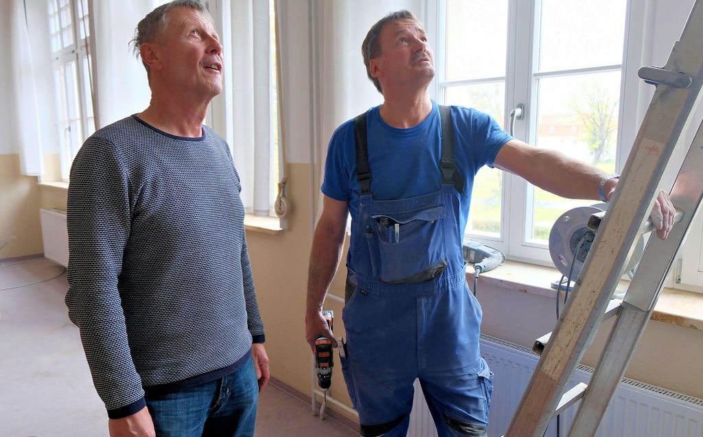 Annaburgs Schulleiter Matthias Weiß und Elektriker Mario Walder schauen sich in einem Unterrichtsraum die fertigen Arbeiten an.