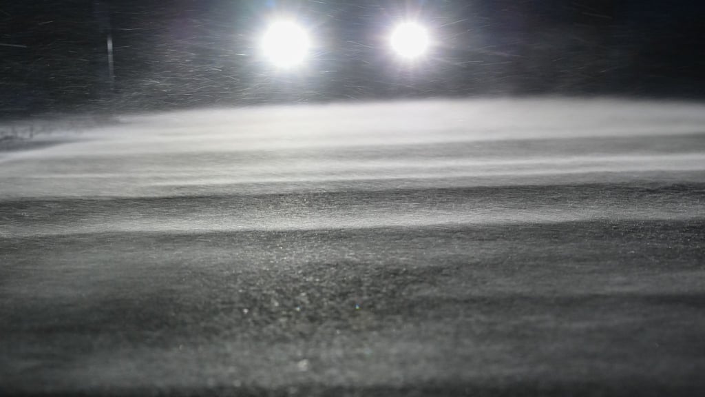 Die Scheinwerfer eines Autos scheinen über eine verschneite Straße.