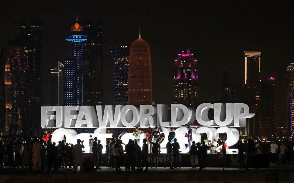 Menschen stehen vor der Eröffnung der WM vor einem beleuchteten Schriftzug „Fifa World Cup Qatar 2022“.