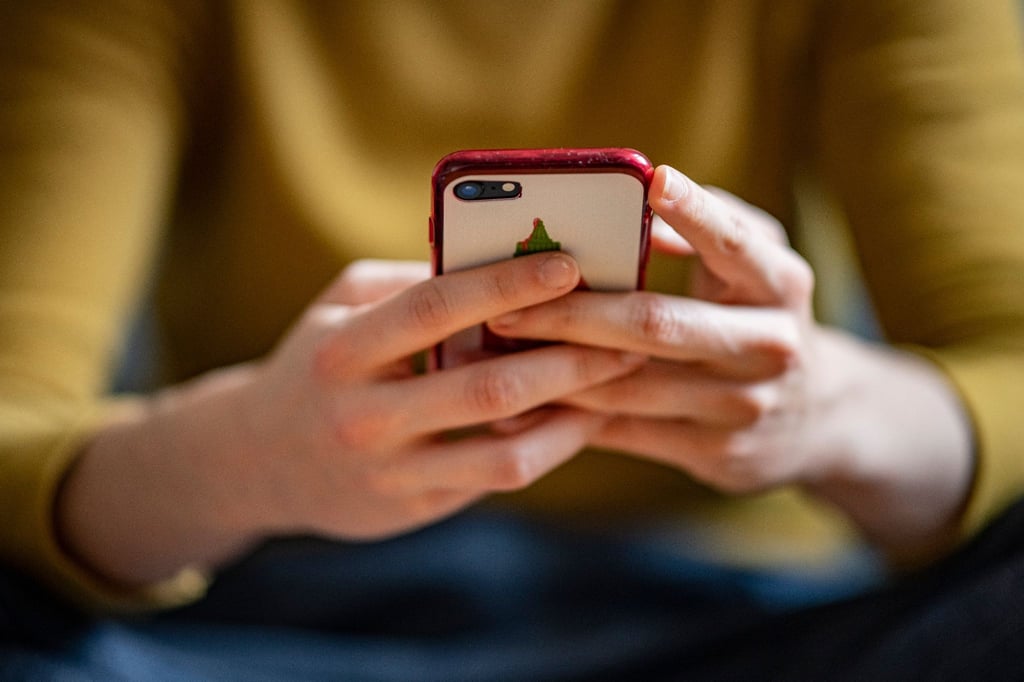 Eine junge Frau hält ein Mobiltelefon in der Hand.