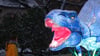 Eine Frau steht in den „Magische Lichterwelten“ im Bergzoo Halle vor einem leuchtenden Dinosaurier.