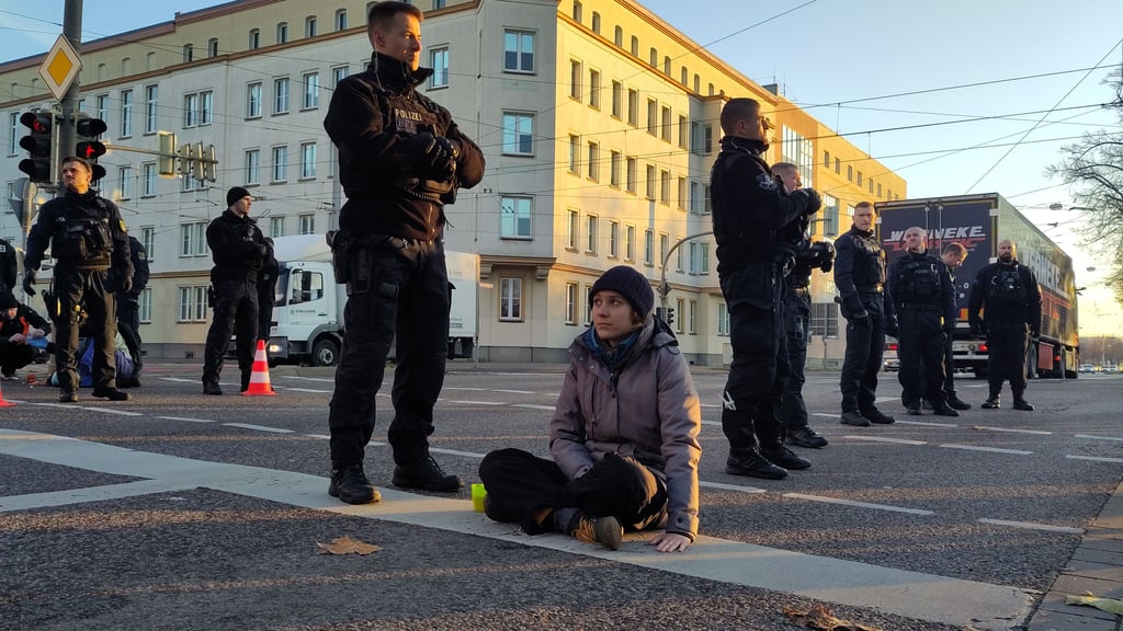 Eine Klimaaktivistin wird mit Öl von der Straße gelöst. Sie hatte sich am 21. November 2022 mit zwei weiteren Personen in Magdeburg auf der B1 festgeklebt. 