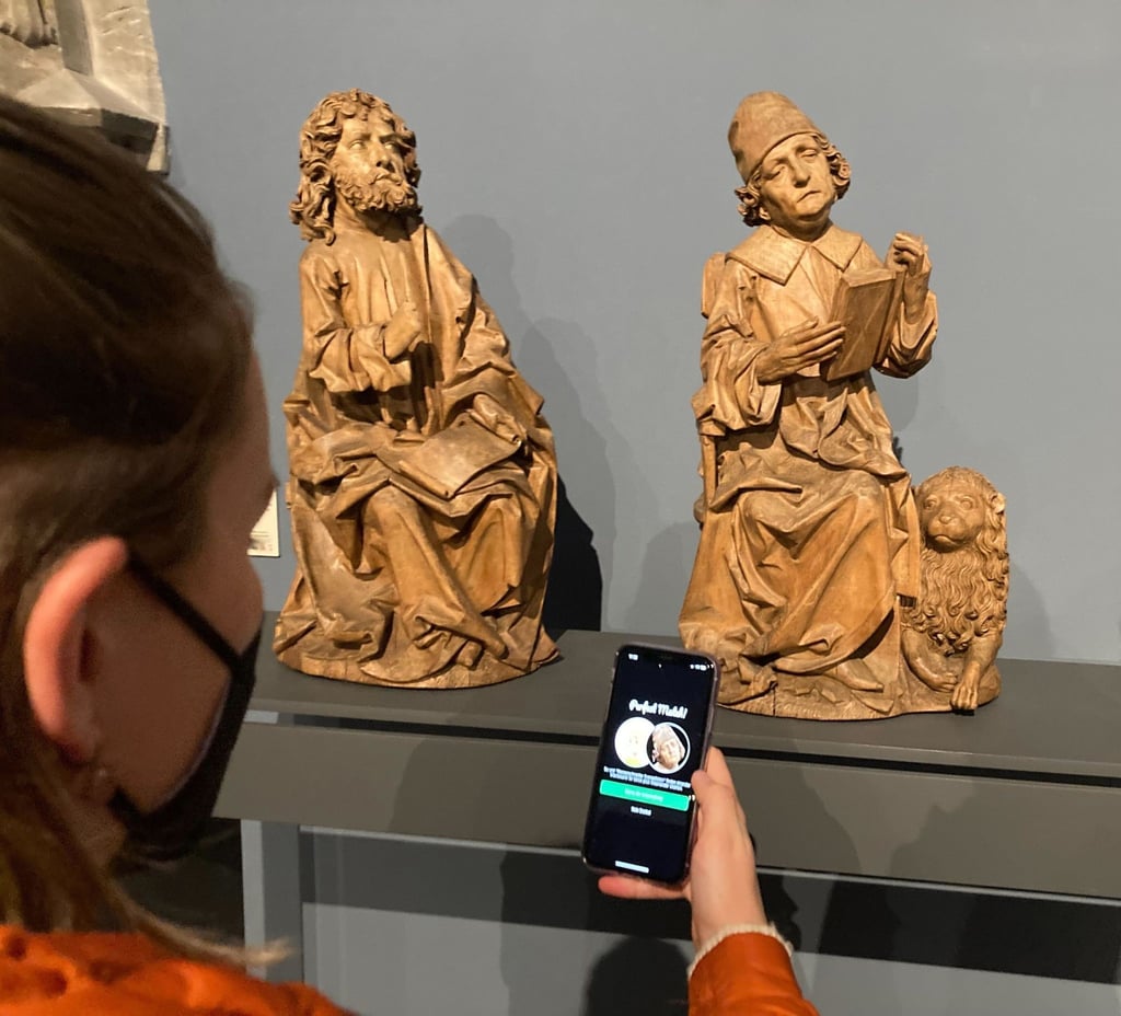 Eine Frau steht im Bode-Museum mit ihrem Handy vor der Figur des Markus (r).