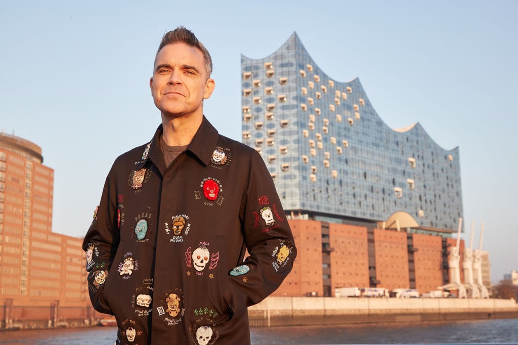 Robbie Williams auf einer Barkasse im Hamburger Hafen. Im Hintergrund ist die Elbphilharmonie zu sehen.
