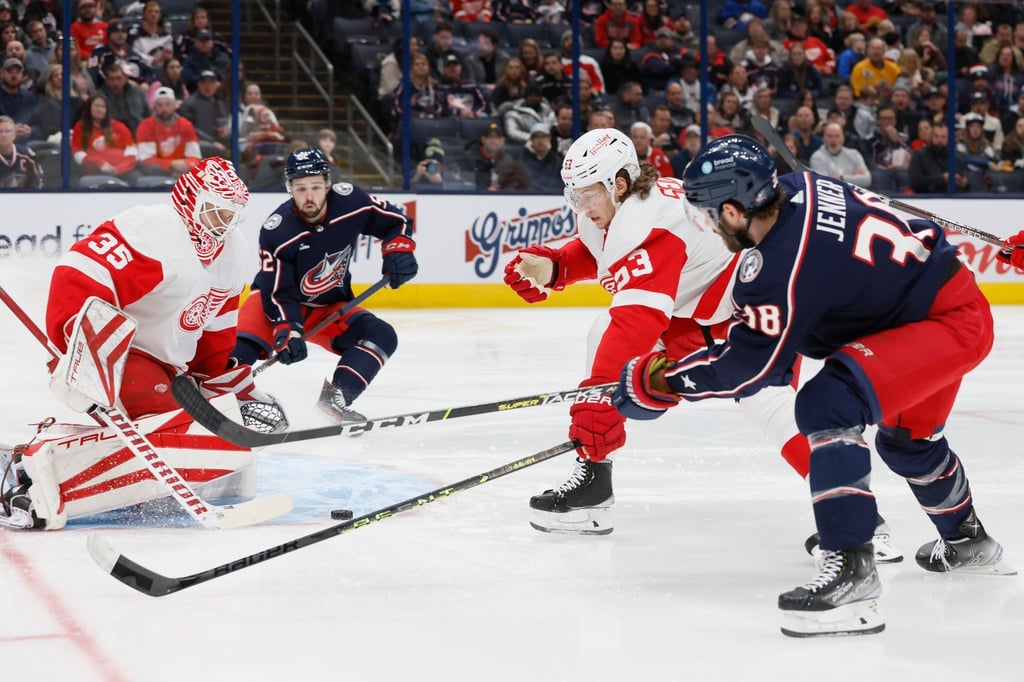 Goalie Ville Husso (l) von den Detroit Red Wings pariert einen Schuss von Teamkollege Moritz Seider (M) gegen Boone Jenner von den Columbus Blue Jackets.