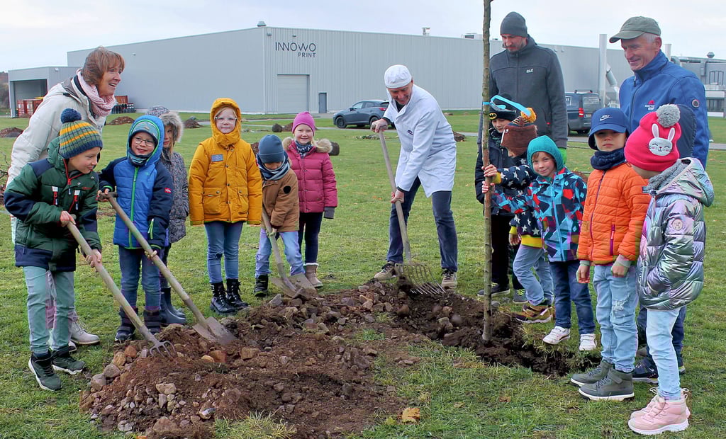 Gemeinsam mit Erstklässlern der Evangelischen Grundschule pflanzen Innowo Print-Chef Bernhard Stradner, Stephan Koppelin und Imker Enrico Kretschmar (hinten von links) den ersten Baum von 35 Bäumen der neuen Streuobstwiese im Gewerbegebiet.