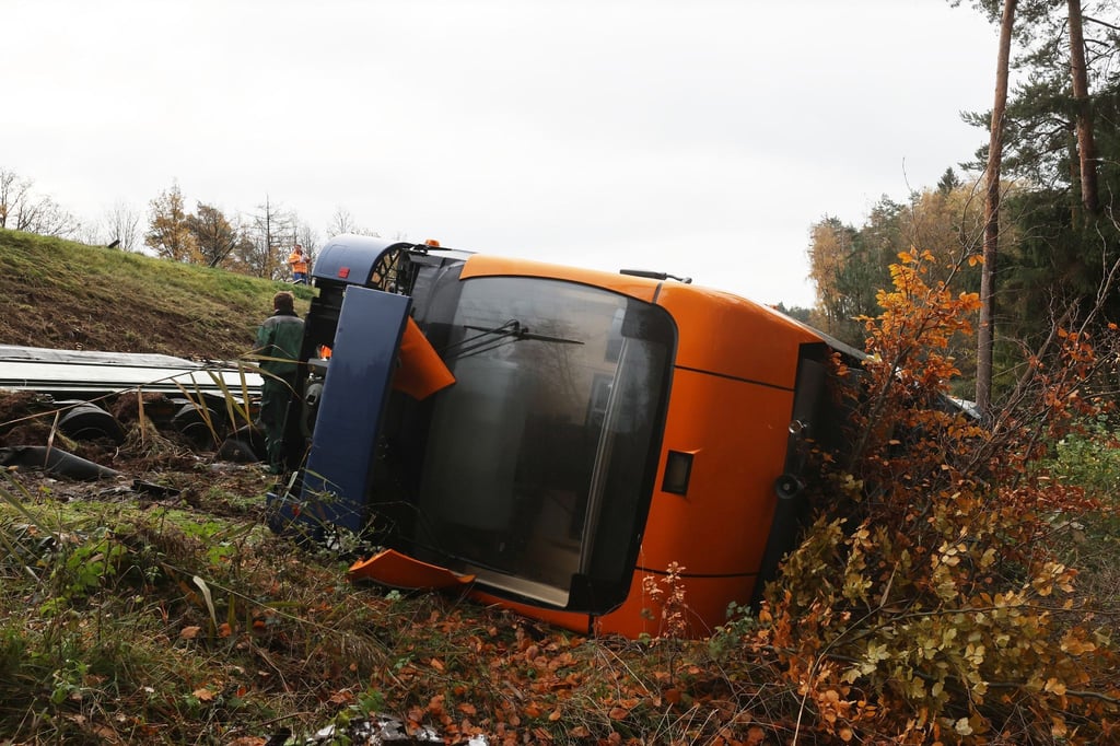 Ein Schwerlasttransporter und ein Straßenbahnwagen liegen unterhalb der Autobahn 9 in einem Graben.