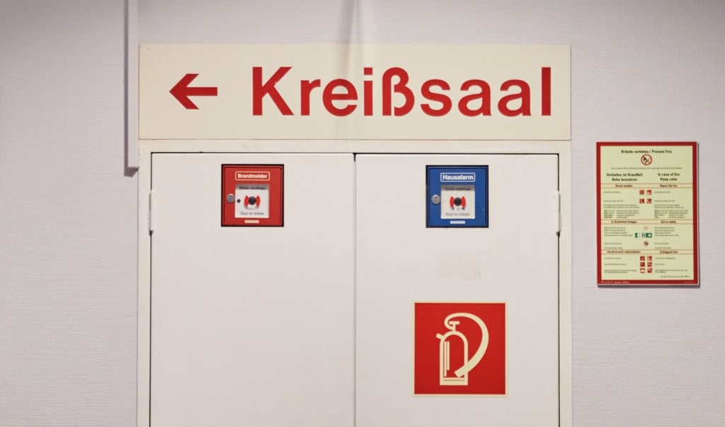 „Kreißsaal“ und ein Richtungspfeil stehen auf einem Schild über einer Tür.