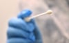 Ein Arzt hält einen Tupfer für einen Abstrich für einen Corona-Test in der Hand.