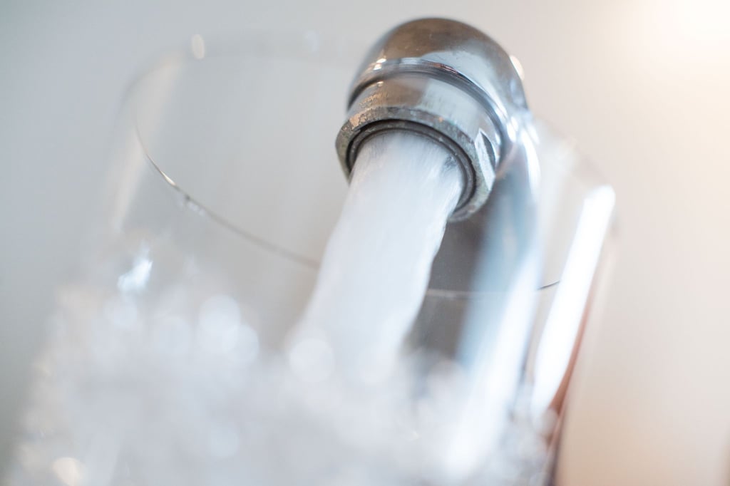 Wasser läuft aus einem Wasserhahn in ein Glas.