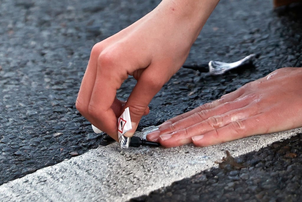 Ein Aktivist von „Letzte Generation“ klebt seine Hand mit Sekundenkleber auf der Straße in Berlin während einer Sitzblockade fest.