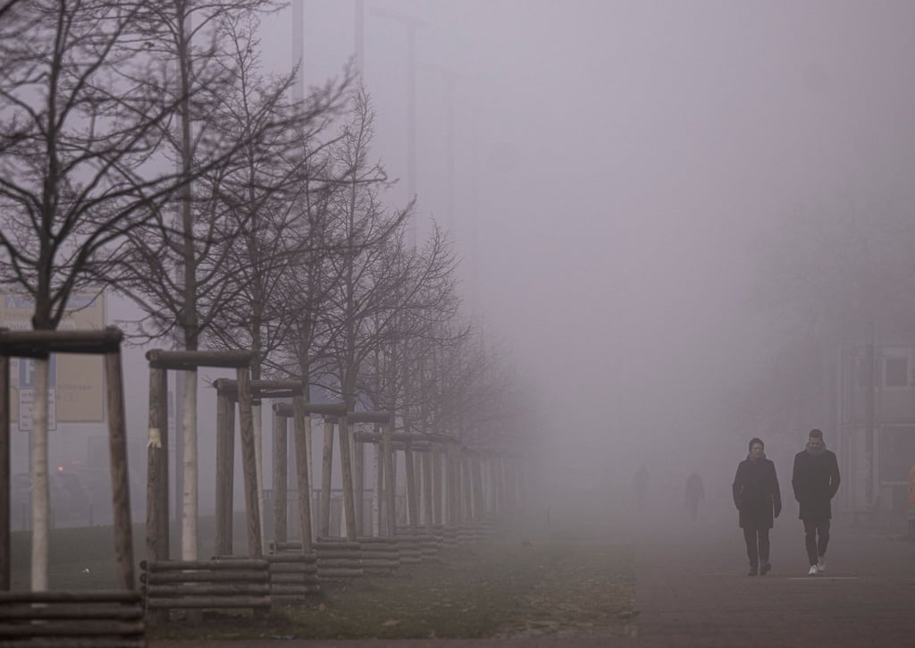 Passanten gehen am Morgen über einen vernebelten Gehweg in Berlin.