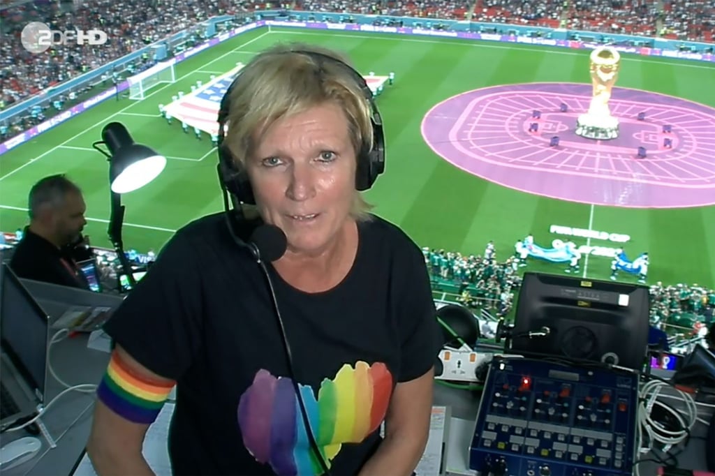 ZDF-Kommentatorin Claudia Neumann mit Regenbogen-Armbinde und einem schwarzen T-Shirt, auf dem ein Herz in den Regenbogenfarben abgebildet ist.
