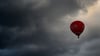 Ein roter Heißluftballon fährt vor dunklen Wolken.