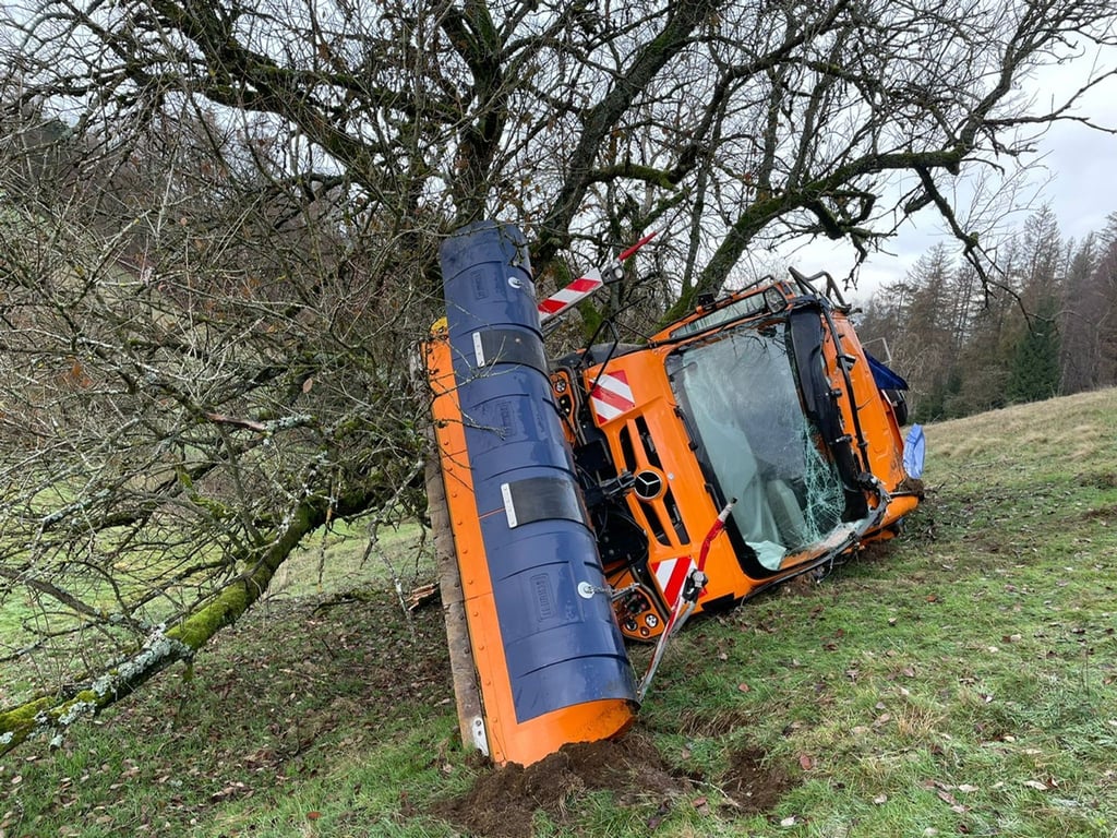 Ein Schneepflug des Winterdienstes ist einen Hang hinabgerutscht und hängt an einem Baum.