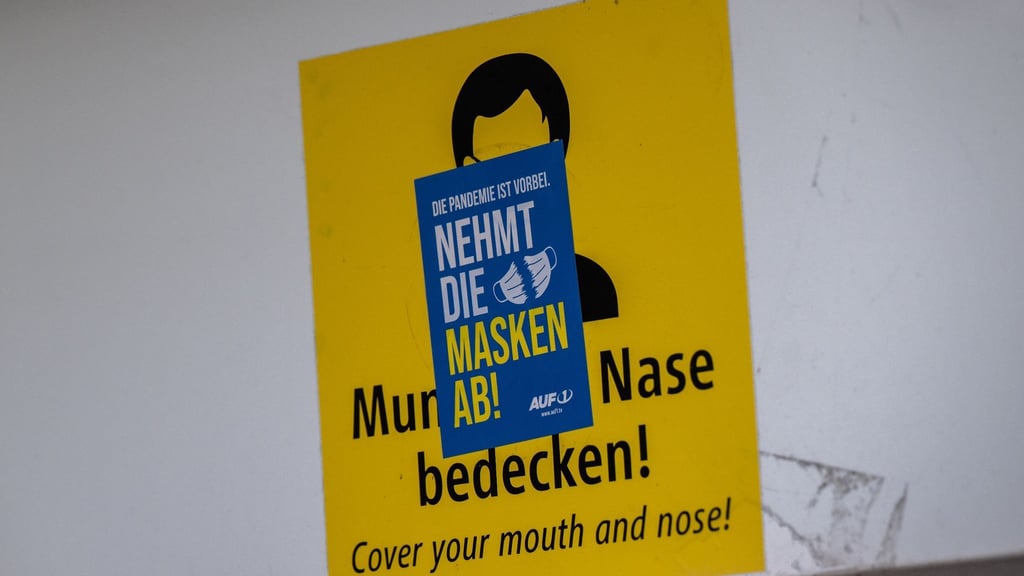 Ein Aufkleber mit der Aufschrift „Nehmt die Masken ab!“ klebt über einem Schild, das zum Tragen einer Mund-Nasen-Maske auffordert. Die Mehrheit der Deutschen ist einer neuen Umfrage zufolge weiter für eine Isolationspflicht für Corona-Infizierte.