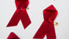 Viele rote Schleifen, das weltweit anerkannte Symbol für die Solidarität mit HIV-Infizierten, liegen auf einem Tisch.