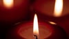 Drei Kerzen brennen in einem dunklen Raum.