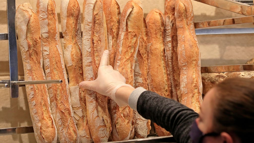 Ein Verkäuferin nimmt ein Baguette aus dem Regal einer Bäckerei.