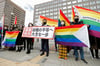Anwälte der Kläger und Unterstützer halten 2021 Regenbogenflaggen und ein Transparent mit der Aufschrift: „Verfassungswidriges Urteil“ vor dem Bezirksgericht Sapporo hoch.