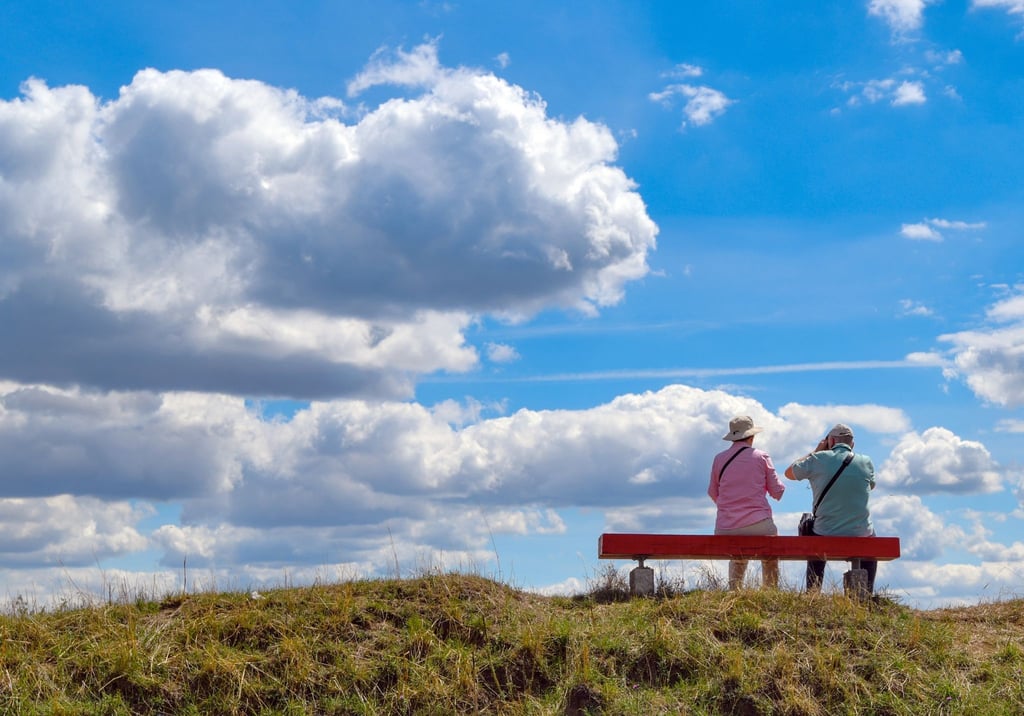 Zwei ältere Menschen sitzen auf einer Bank in der Natur.