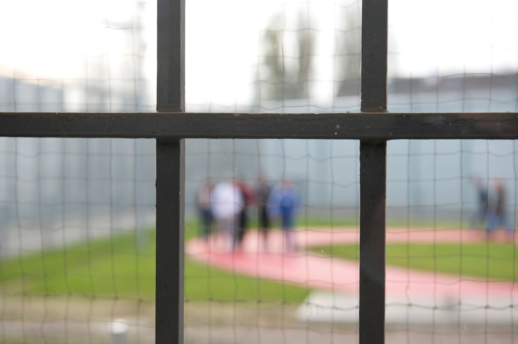 Hinter einem Gitter laufen Gefängnisinsassen über einen Gefängnishof.