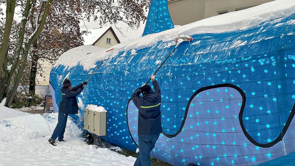 Mit Besen befreien Mitarbeiter des Bergzoos den Urzeit-Hai und andere Figuren der „Magischen Lichterwelten“ auf dem Reilsberg von Schnee.