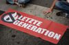 Aktivisten der Gruppe „Letzte Generation“ haben sich hinter einem Banner mit ihrem Logo festgeklebt.