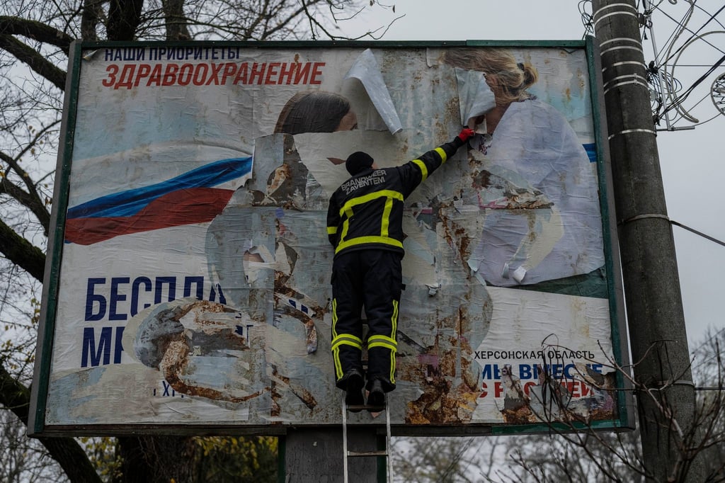 Ein ukrainischer Feuerwehrmann reißt in der kürzlich befreiten Stadt Cherson ein russisches Werbeplakat von einer Werbetafel.