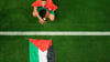 Marokkos Abdelhamid Sabiri feiert neben einer palästinensischen Flagge auf dem Rasen hockend den Sieg seiner Mannschaft.