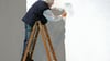 Ein Rentner streicht eine Wand.
