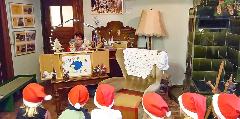 Gabriele Schober spielt Gernröder Kita-Kindern am Kachelofen der Alten Elementarschule das Märchen vom Tannenzapfenkönig vor.