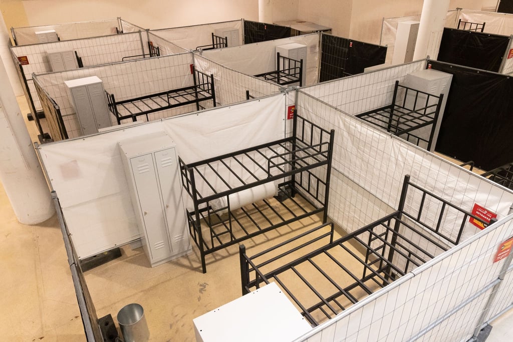 Stockbetten und Spinde stehen zwischen Sichtschutzzäunen in einer Flüchtlingsunterkunft.
