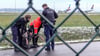 Die Bundespolizei und ein Sicherheitsmitarbeiter steht mit einem sichergestellten Bolzenschneider an einem Zaun.