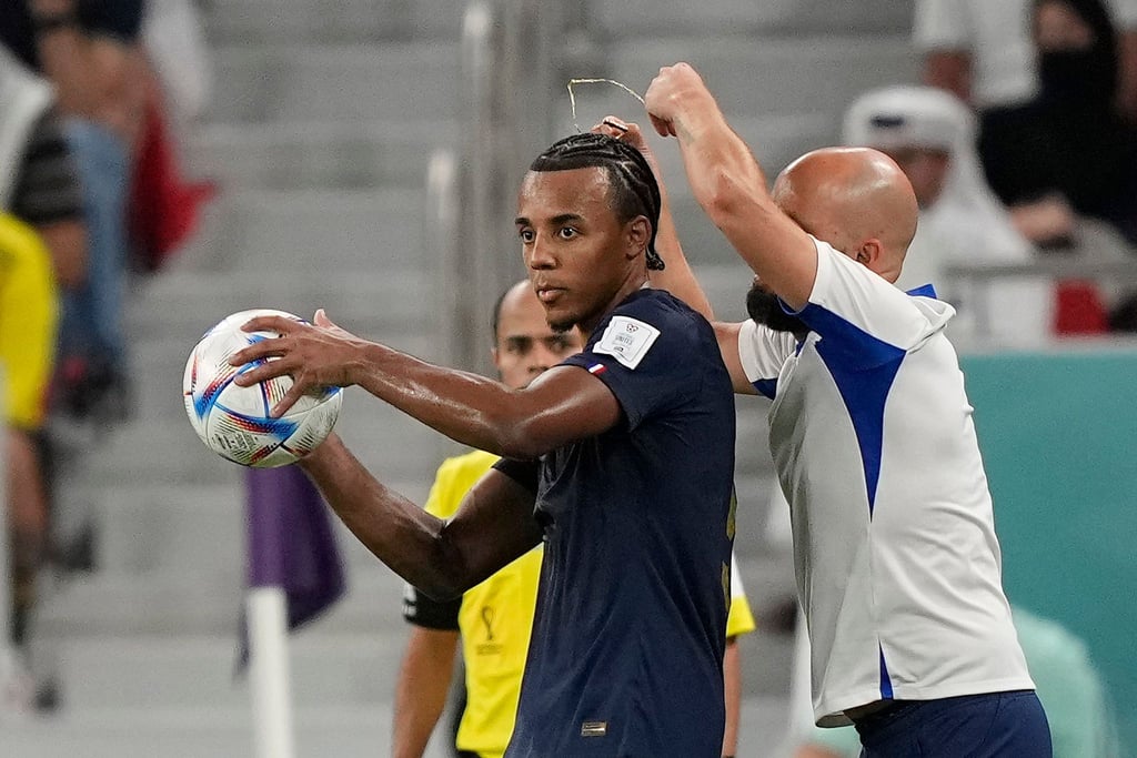 Ein Assistenztrainer nimmt dem französischen Nationalspieler Jules Kounde während des Spiels die golende Halskette ab.