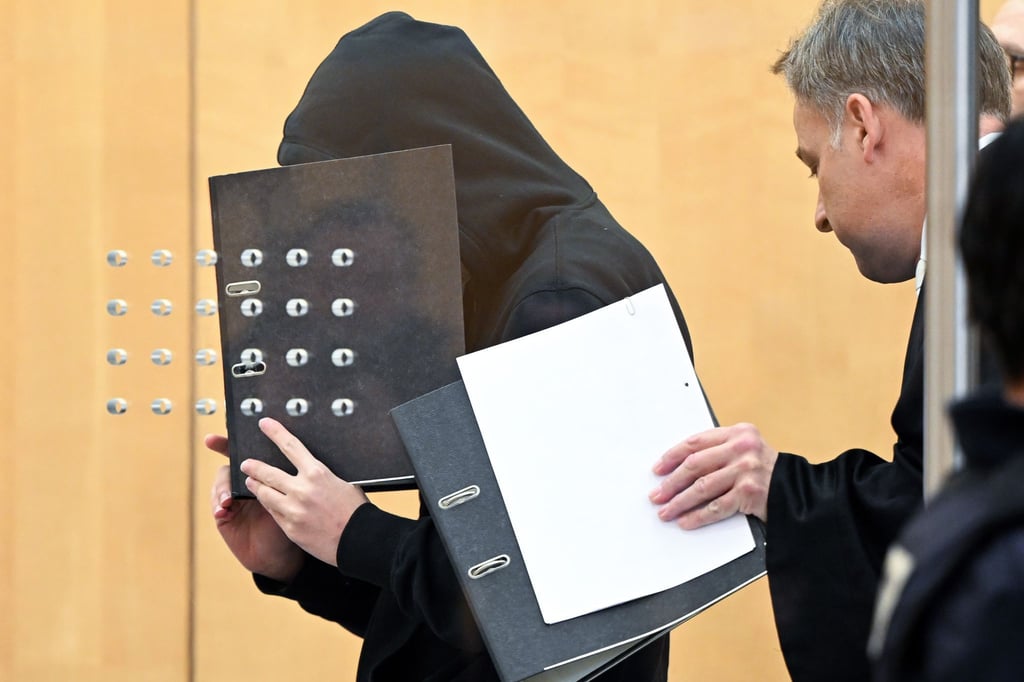Der Angeklagte (l) verdeckt mit einem Aktenordner sein Gesicht, als er mit seinem Verteidiger zu Beginn der Verhandlung in einem Saal am Oberlandesgericht eintrifft.