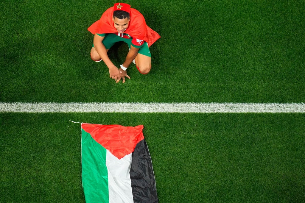 Marokkos Abdelhamid Sabiri feiert neben einer palästinensischen Flagge auf dem Rasen hockend den Sieg seiner Mannschaft.