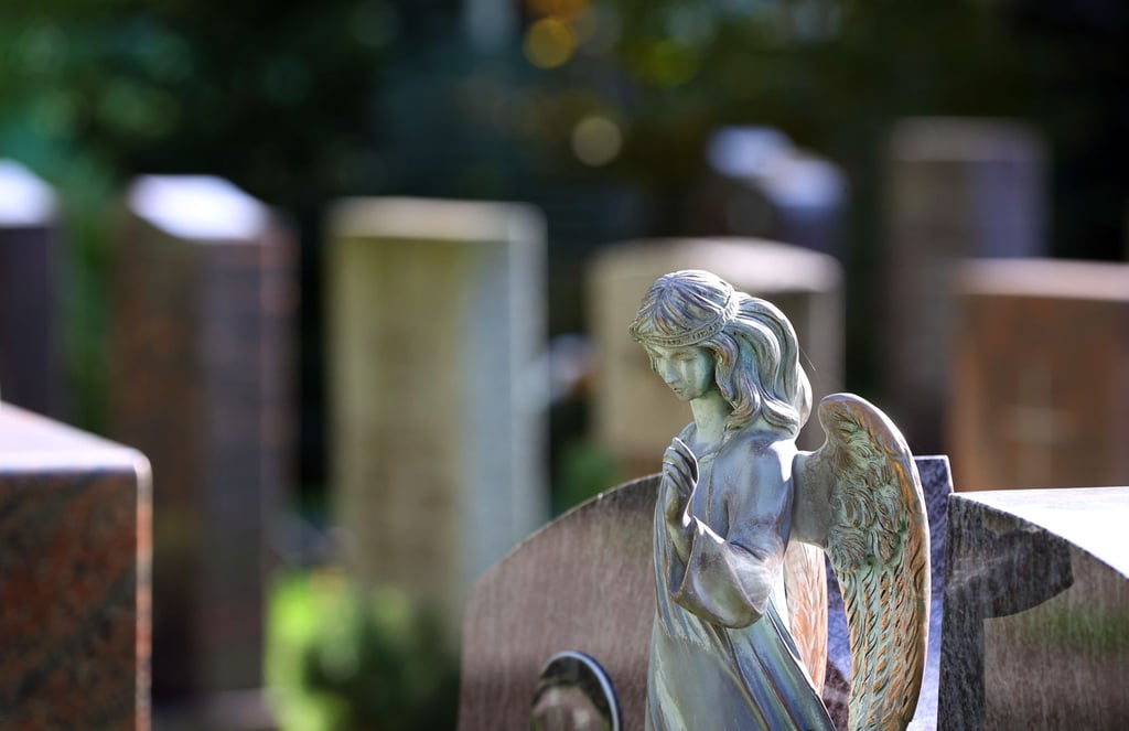 Eine Engelsfigur steht auf einem Friedhof vor Grabsteinen.