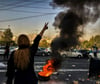 Eine Frau steht während einer Demonstration nach dem Tod der 22-jährigen Mahsa Amini vor einem brennenden Autoreifen und zeigt das Victory-Zeichen.