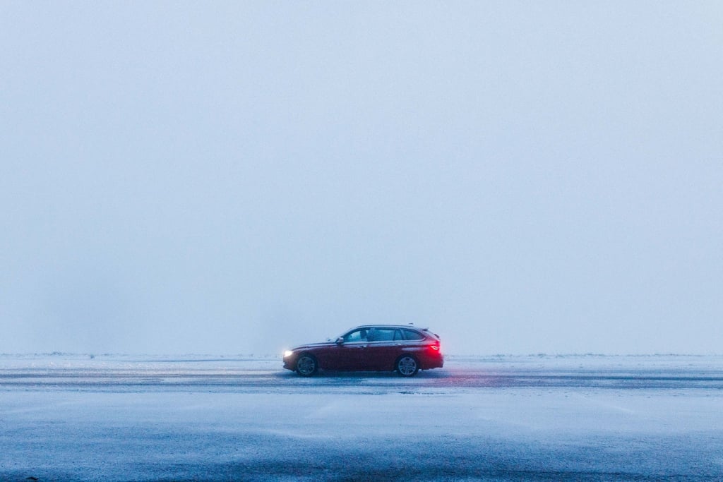 Ein Auto fährt bei dichtem Nebel über eine schneebedeckte Straße.