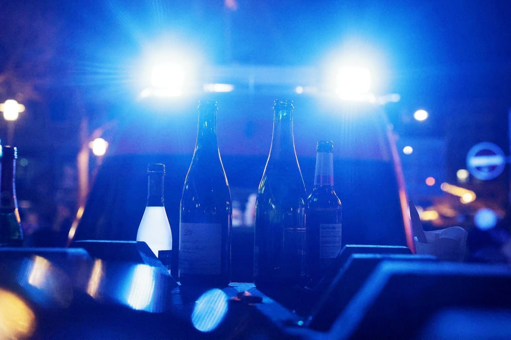 Leere Flaschen, die vorher mit alkoholischen Getränken gefüllt waren, stehen vor einem Krankenwagen mit eingeschaltetem Blaulicht.